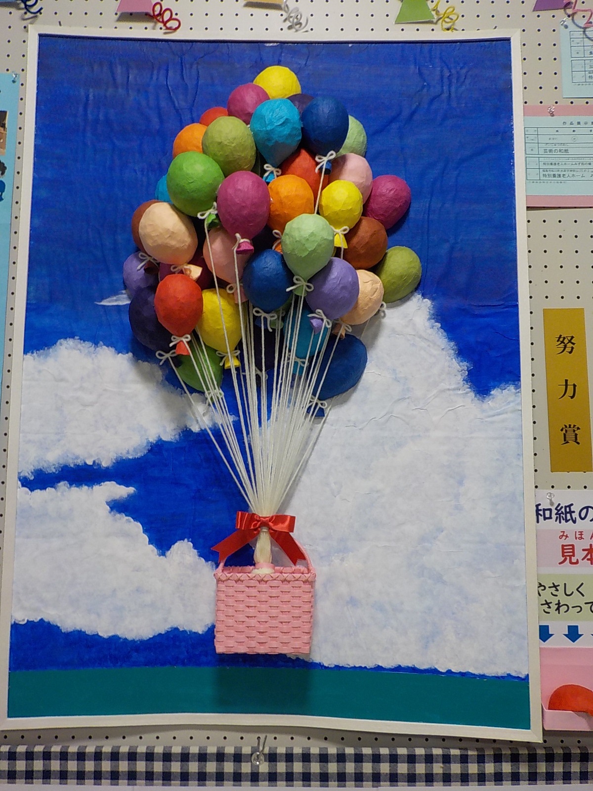 海の上をピンク色のカゴに赤色のリボンで結んだ沢山のカラフルな色の風船が空を飛んでいく様子を描いた努力賞受賞作品の写真