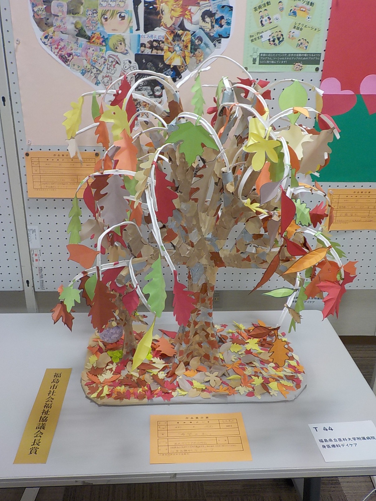 赤やオレンジ色などの葉が紙で作られた一本の木の枝や落ち葉で表現された福島市社会福祉協議会長賞受賞作品の写真