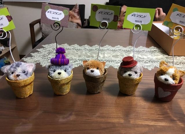 5つの鉢の中からそれぞれ犬が顔を出し、背後に設置された針金で作られたメモを挟むメモスタンドの写真