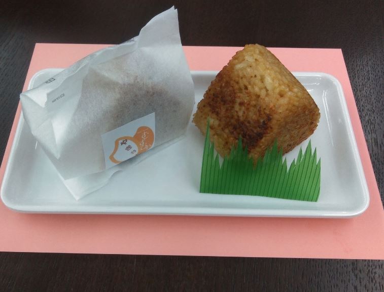 白色のトレーの上に「やきおに」と書かれた袋に入ったおにぎりと、三角形で全体が茶色のおにぎりが置かれている写真