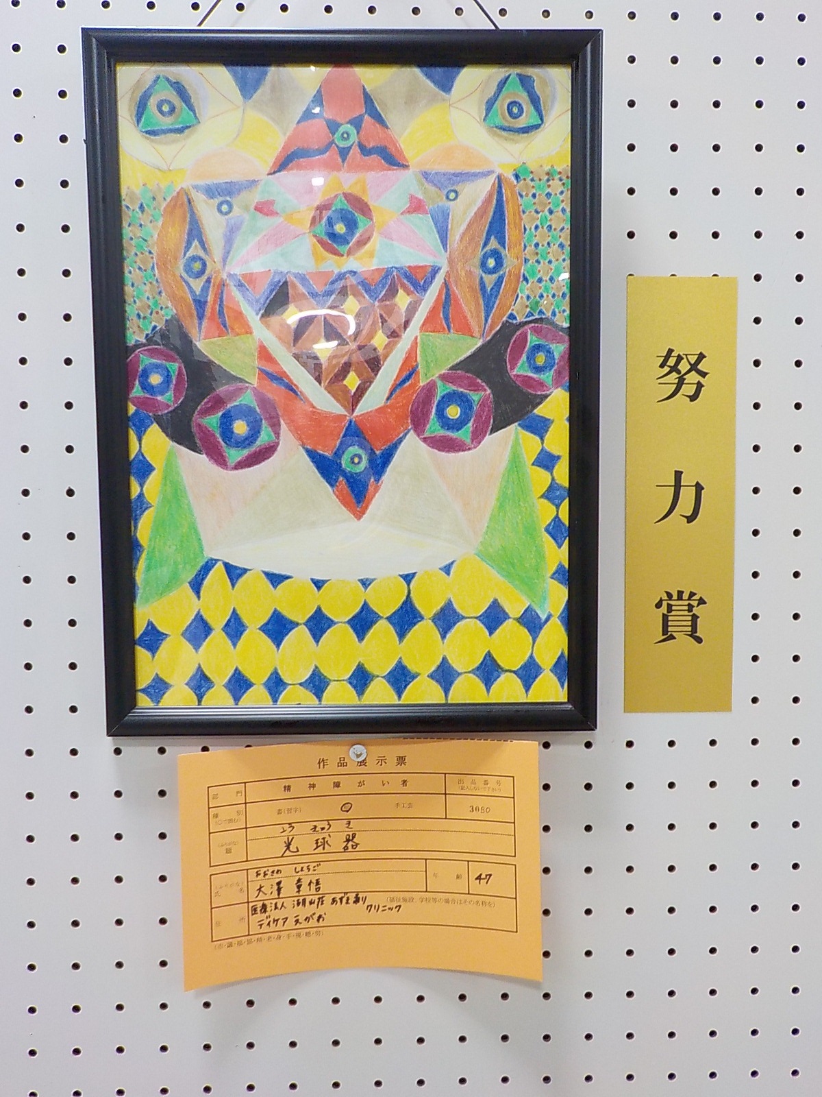 両端の上に円形の中に三角形と二重丸、中央に円形の中に四角形と二重丸がカラフルな色で描かれた「光球器」と題した努力賞受賞作品の写真