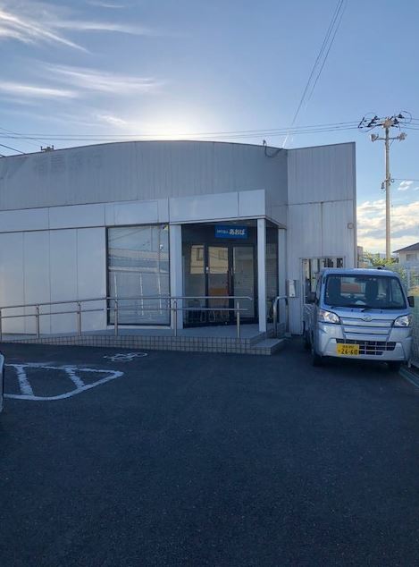 シルバーの軽乗用車が停車している入り口前にスロープが設置された白壁の事業所の建物外観の写真