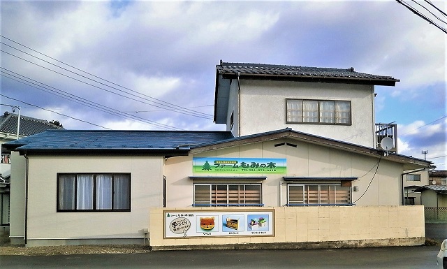 左半分は1階右半分は2階建てで白壁に「ファームもみの木」と書かれた看板が設置された建物外観の写真