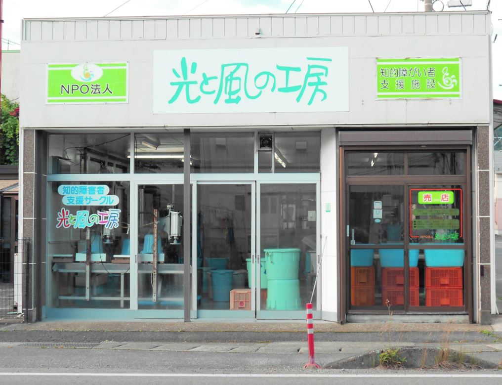 道路に面した側はガラス張りで「光と風の工房」と書かれた看板が設置された事業所の写真