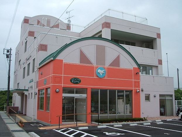 3階建てで薄いピンク色の外壁、入り口はオレンジ色の外壁をした新おおぞらの夢の建物外観の写真