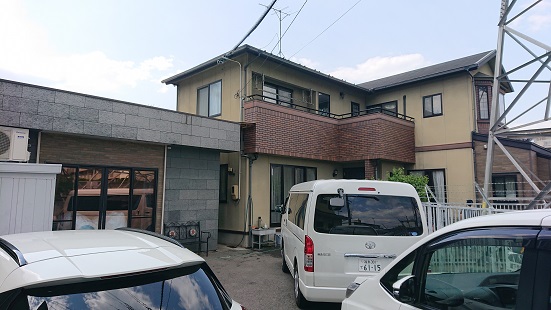 敷地内に3台の車が停まっているグレー色のレンガ調の建物外観の写真