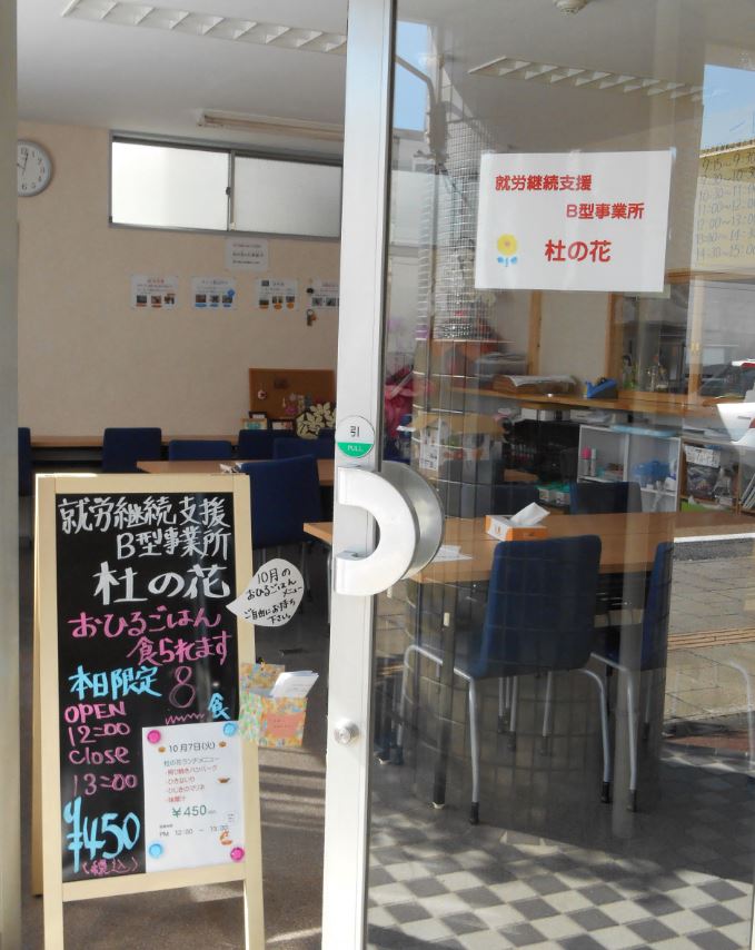 事業所名「杜の花」やメニューなどが書かれた立て看板が扉を開けた入り口に設置された写真