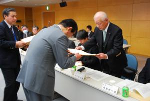 長机を挟んで向かい合って立っているスーツ姿の2名の男性が協定書を取り交わしている福祉避難所協定締結式の様子の写真