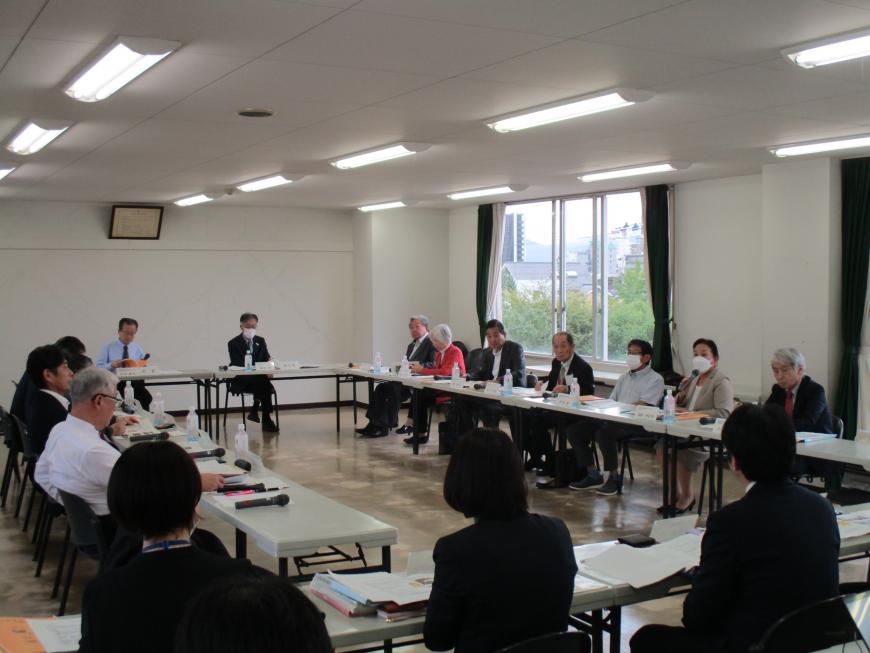 口の字型に並んだ白い会議机の席に、たくさんの出席者が座って話し合いをしている協議会の様子の写真