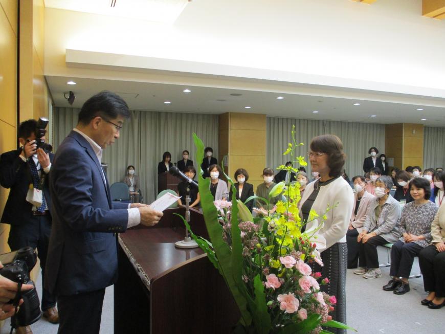 演台の後ろに立った市長が出席者に向かって書状を読み上げている様子の写真