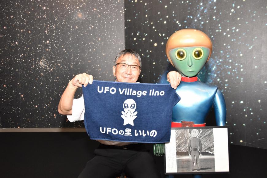 近野さんが「UFOの里 いいの」と書かれたタオルを持っている写真