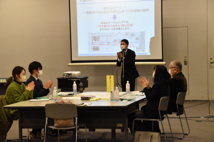 前のスクリーンに資料が写し出され指や手をたたきながらゲームをする参加者達の写真
