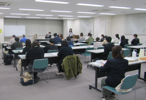 2人1組のテーブルと椅子が設置された会場で会議の様子全体を後ろから撮影した写真