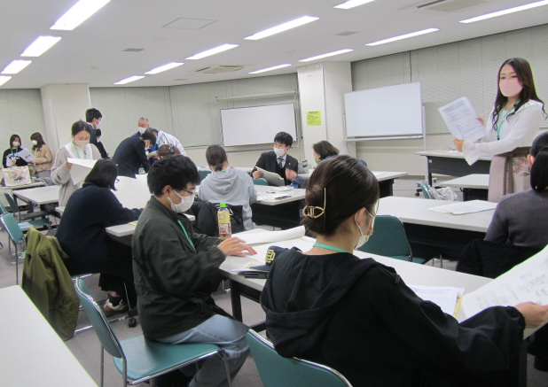 女性が立って資料を見せながら話をするのを座って聞いている参加者達の写真