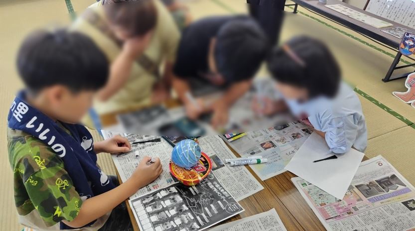 テーブルに新聞が敷かれ子供達がイベントに参加する様子にモザイクのかかった写真