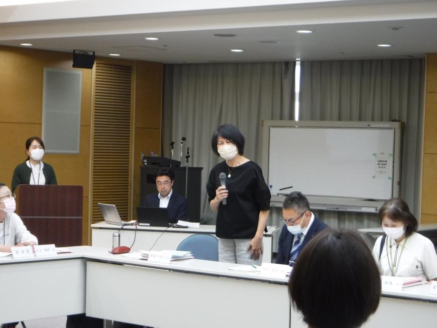 自席から立ち上がった女性が右手にマイクを持ち話をしている写真