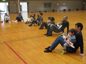 後ろに両手をついた保護者の膝の上に前向きで乗っている子どもの写真