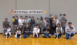 「親子ふれあい・からだあそび」と書かれた横断幕の前で参加した親子が記念撮影を行っている写真