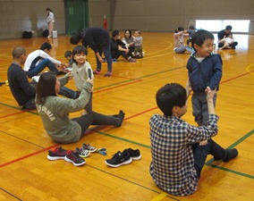 床に座った保護者の膝の上に手で支えてもらいながら子どもが立っている様子の写真
