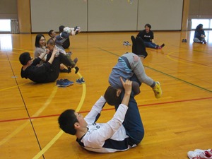 仰向けになっている保護者の足につかまり手で支えてもらいながら前転をしようとしている子どもの写真