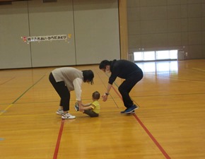 子どもの両足を持った保護者が後方に引っ張っておりもう一人の参加者が子どもの背中側から手で支えるような姿勢をとっている写真