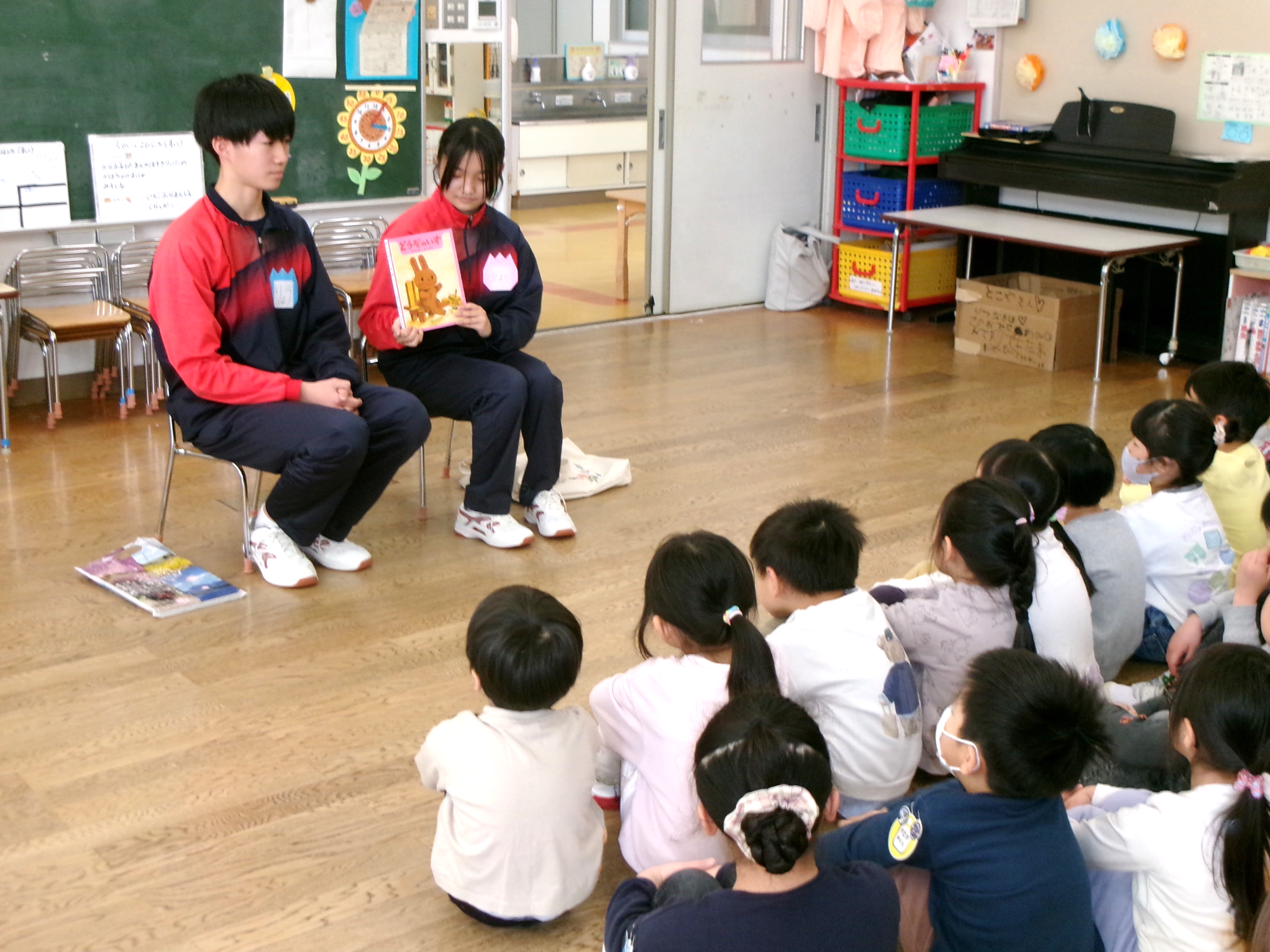 兵庫県立鳴尾高等学校の学生さん2人が、子供たちの前で本の読み聞かせを行っている写真。