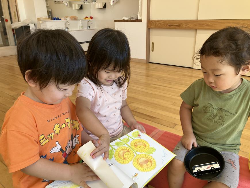 ひまわりの絵が載った絵本のページを3人の子供たちが楽しそうに見ている写真