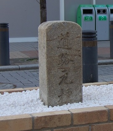 レンガで造られ白の小石が敷き詰められた上に「道路元標」と刻まれた標石の写真