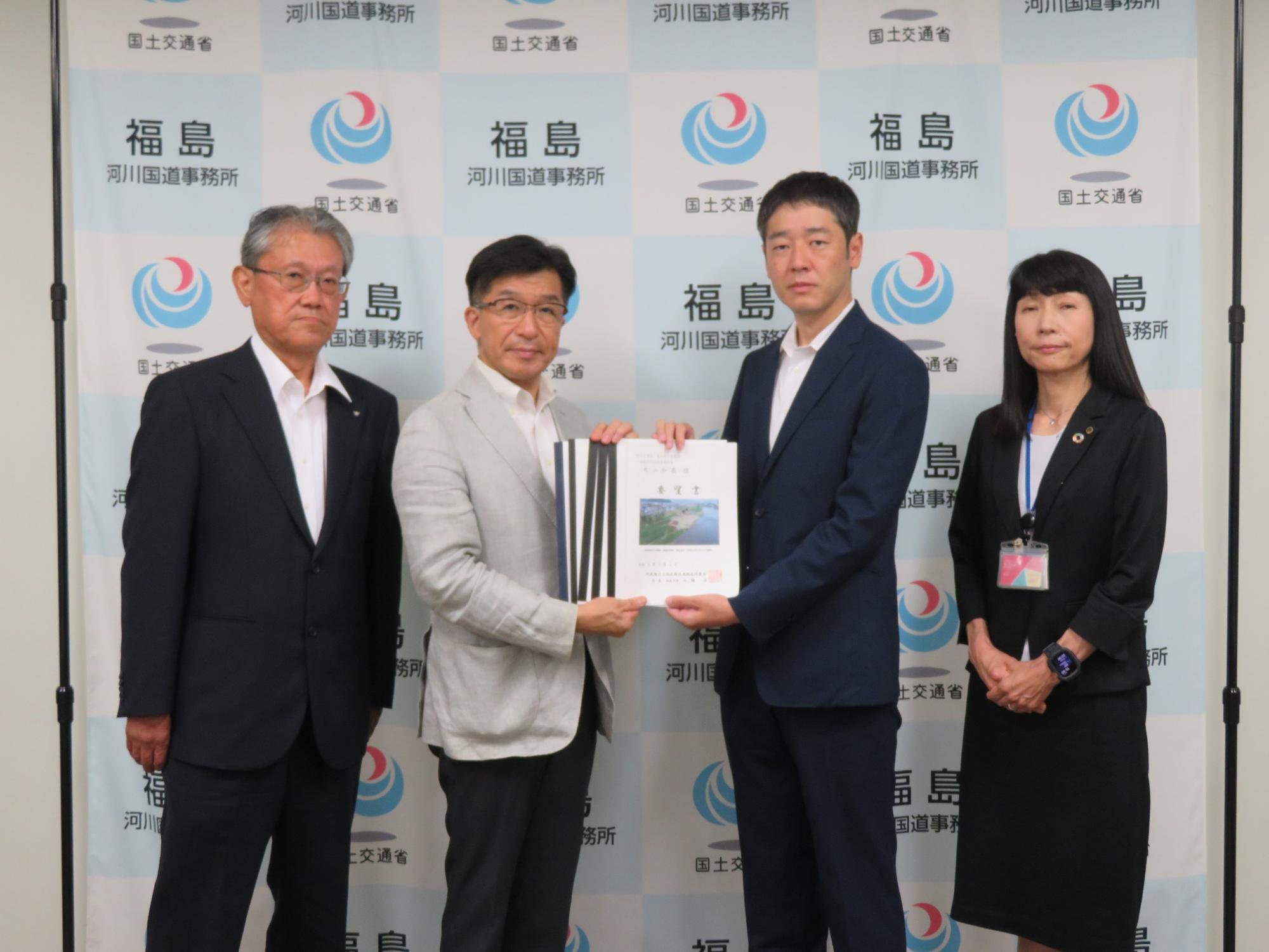 福島のバックボードの前で4人の方が横一列に並び中央に福島市長と丸山和基事務所長が要望書を持ち記念撮影をしている写真