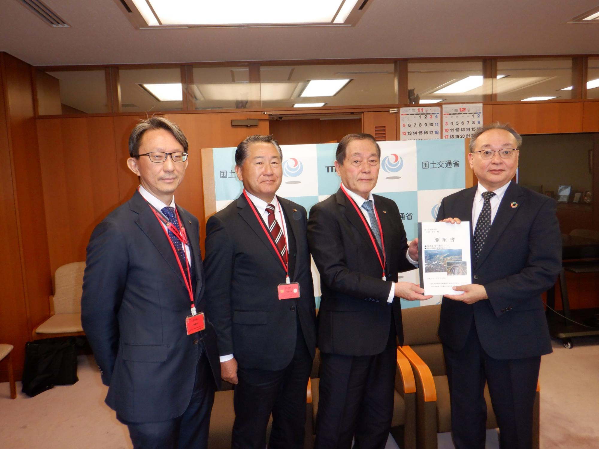 吉岡幹夫技監と渡邊博美福島商工会議所会頭が要望書を持ち4人の方が横一列になり記念撮影をしている写真