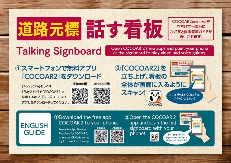 QRコードなどが書かれ携帯でダウンロードする方法を日本語と英語で説明している道路元標 話す看板の写真