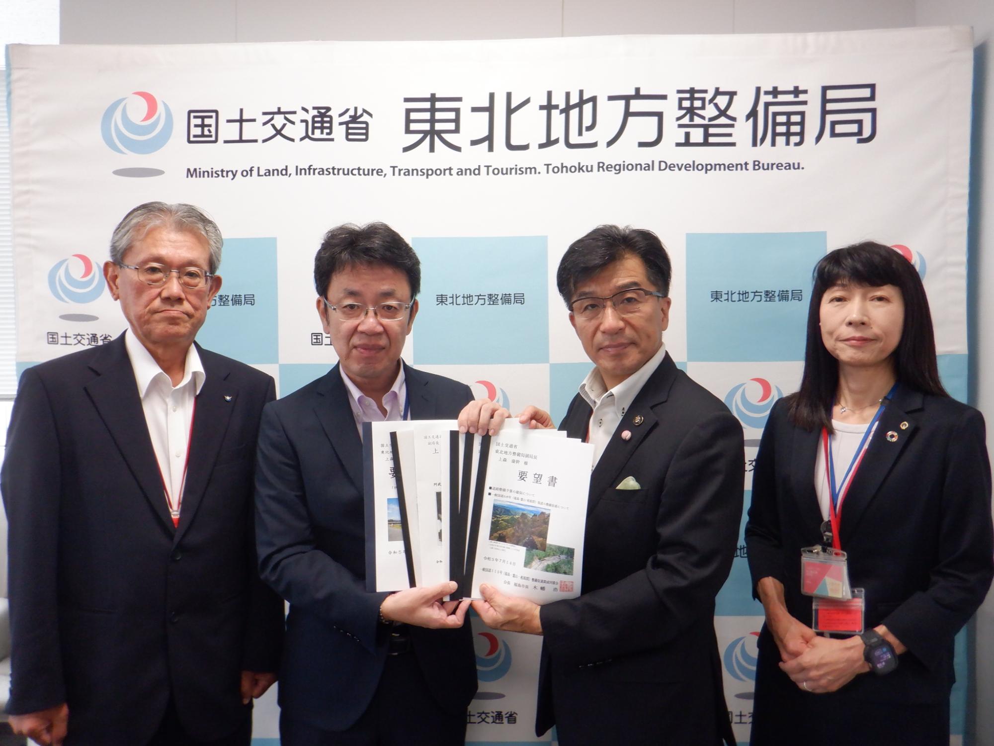 国土交通省 東北地方整備局と書かれたバックボードの前で4人の方が横一列に並び中央に上森康幹副局長と福島市長が要望書を持ち記念撮影をしている写真