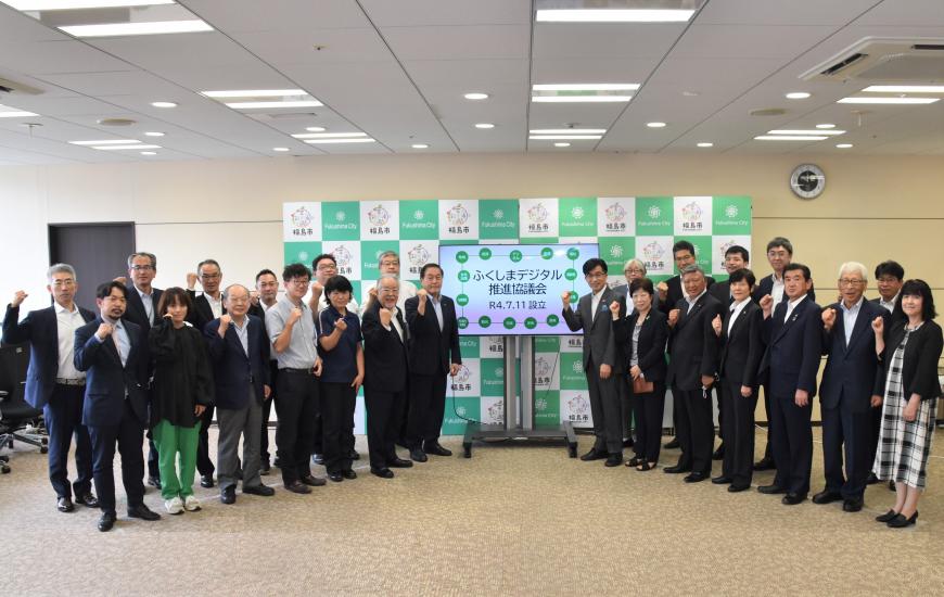 「ふくしまデジタル推進協議会」と書かれた大型モニターの両側にガッツポーズをした関係者が扇状に並んでいる写真