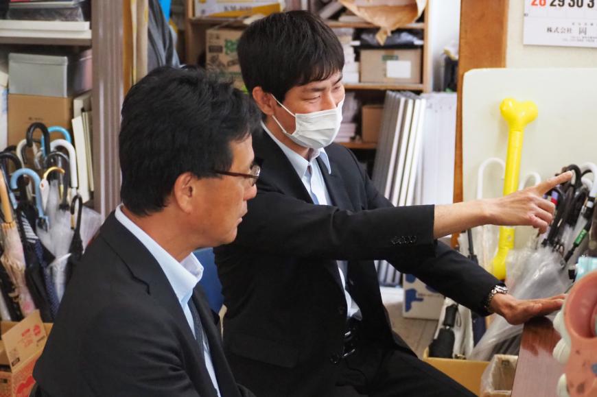 スーツ姿の根本さんが社員の男性と横に並んで座り、画面を指差して説明を行っている様子の写真