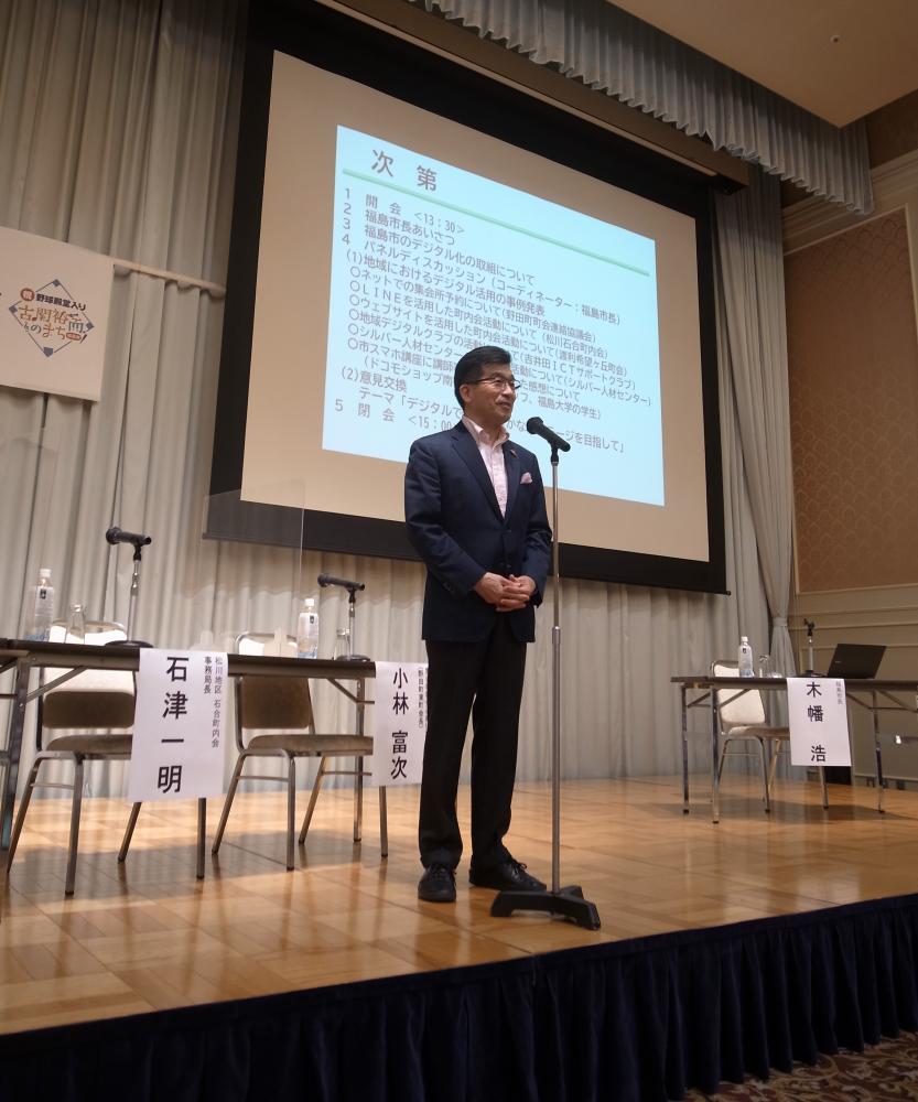 前方に資料が映し出されたスクリーンが設置されたステージ上で、マイクの前に立つ市長が話をしている写真