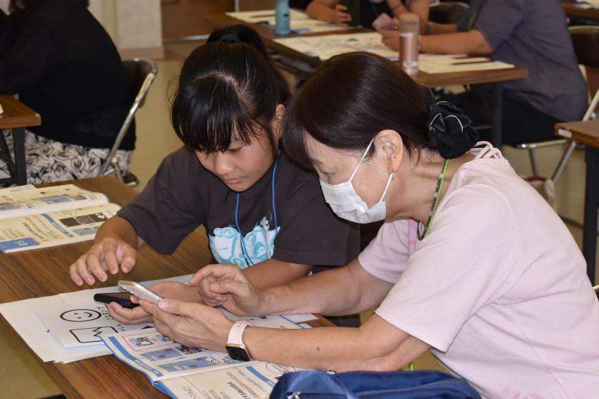 スマートフォンを持って操作している祖母に説明している女の子の写真