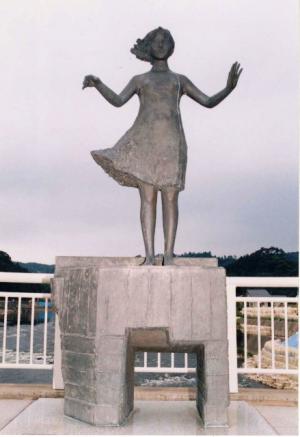 両手を横にあげた女の子の髪が風でなびいている作品「西風の防波堤」の写真