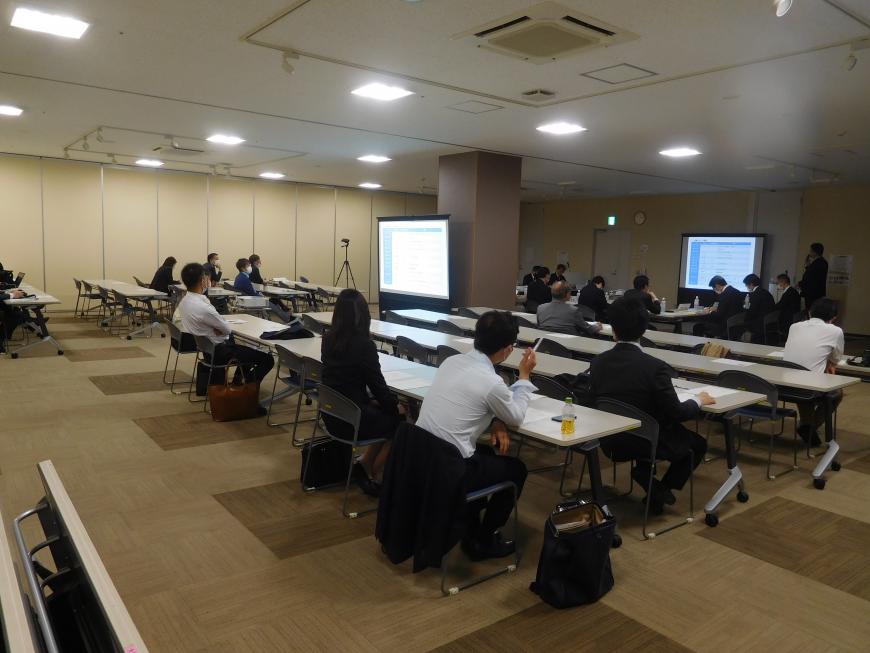 前方と真ん中の2ケ所にモニターが設置され参加者の人たちが説明を聞いている写真