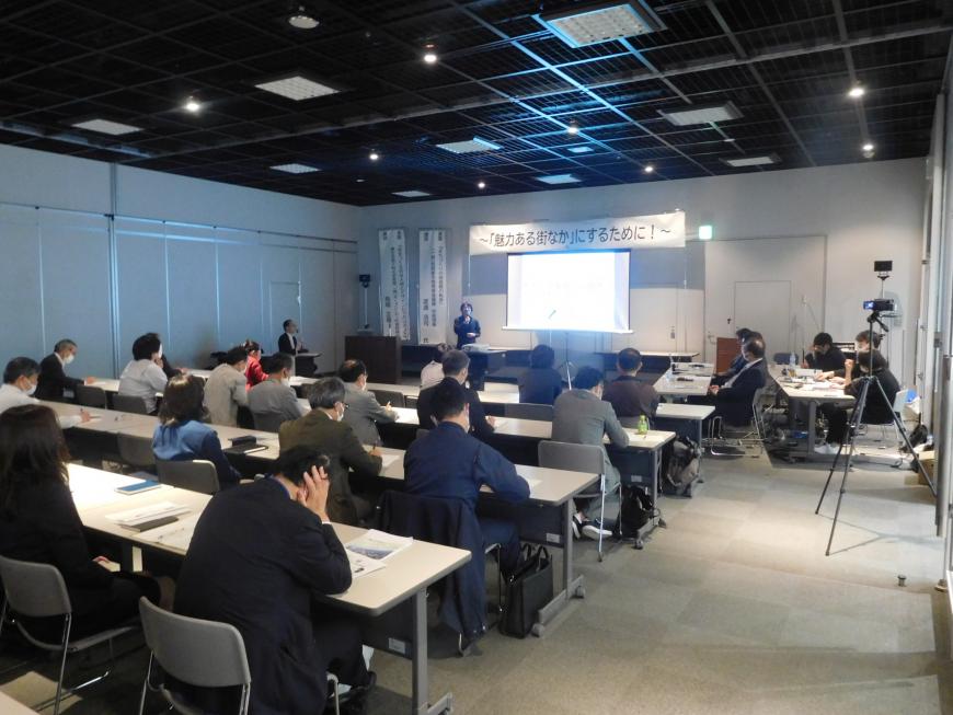 スクリーンの上に「魅力ある街なか」にするために!の幕が張られ演台に立つ馬場氏が講演をしている様子を写した写真