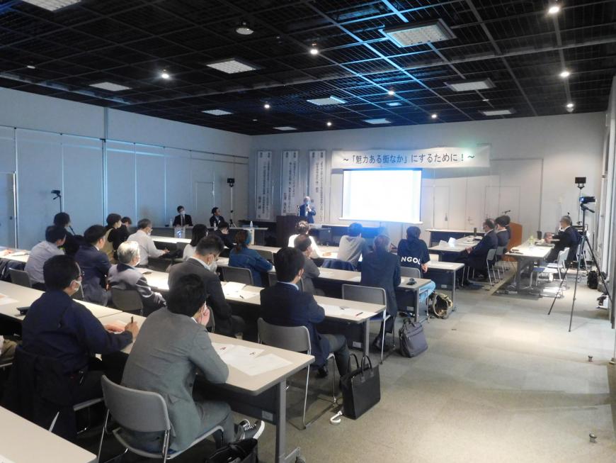 スクリーンの上に「魅力ある街なか」にするために!の幕が張られ演台に立つ柳氏が講演をしている様子を写した写真