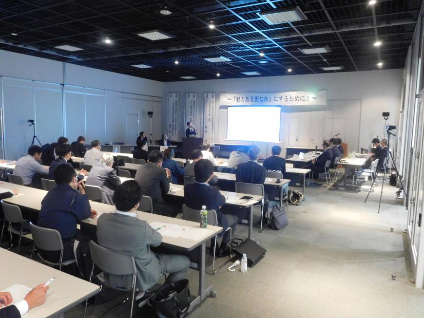 スクリーンの上に「魅力ある街なか」にするために!の幕が張られ演台に立つ福井氏が講演をしている様子を写した写真