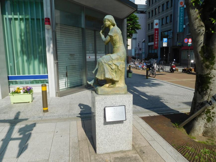 歩道上に立つ一本の木の傍にある女性が髪を手入れしている作品「霽(は)れ」の写真