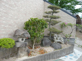 石灯篭や鳥の置物が置かれ、松など木が植栽されている庭園の一部の写真