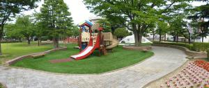 遊歩道の中心に緑色の芝生と滑り台などの遊具が設置されている新浜公園の全体写真