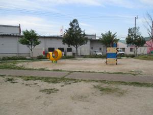 砂地になっている広場に黄色の遊具やかべのぼりの遊具が設置されている公園内の写真