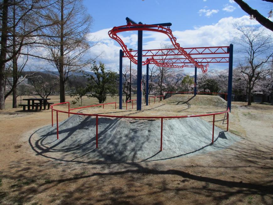周りを木に囲まれ、赤と青の配色の大型遊具が設置された蓬莱中央公園内の写真