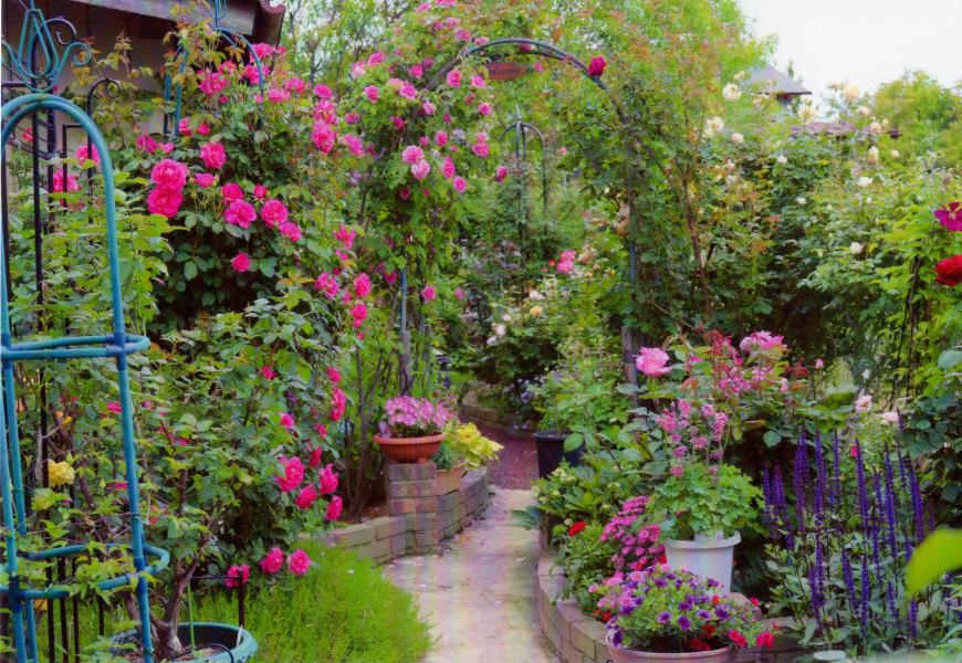 奥まで続く庭の小道の両脇に四季折々の色とりどりの花がたくさん咲いている写真