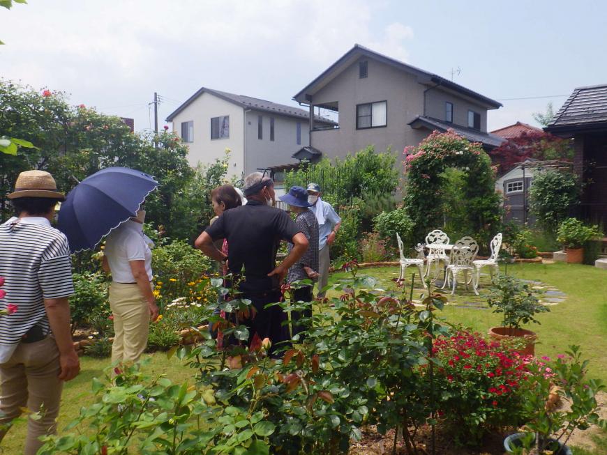 白いテーブルと椅子が4脚置かれ周りを手入れがされた草花が咲いている庭に複数名が見学にきている様子の写真