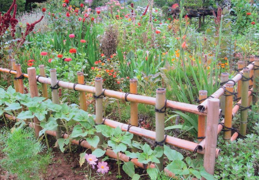 竹で作られた柵の中で赤や黄色などの四季折々の花が植えられている庭の写真