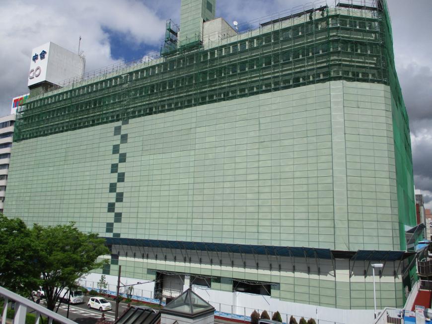 建物全体がネットで覆われ、上階から解体作業が進んでいる様子の写真
